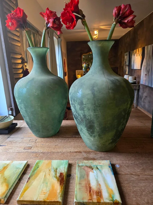 Twee groene vazen met rode amaryllissen, op tafel drie kleine doeken.